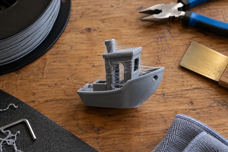 Model z 3D tiskárny s jemnými pavučinami a nitkováním mezi sloupky.