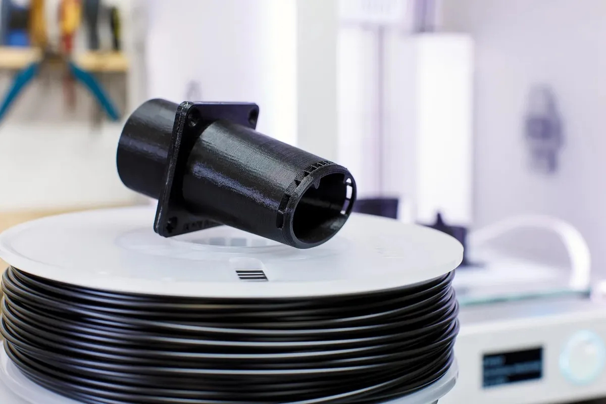 Černý vytištěný díl na cívce filamentu pro Original Prusa MINI+