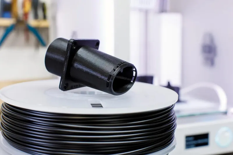 Černý vytištěný díl na cívce filamentu pro Original Prusa MINI+