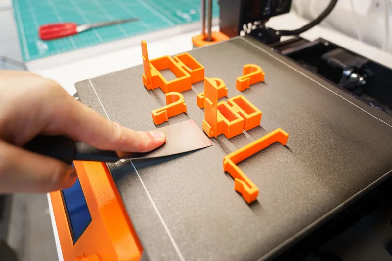 Oranžové modely na podložce stolní FDM 3D tiskárny po tisku
